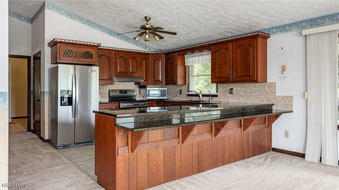 Kitchen featuring tasteful backsplash, appliances with stainless steel finishes, dark stone countertops, and kitchen peninsula