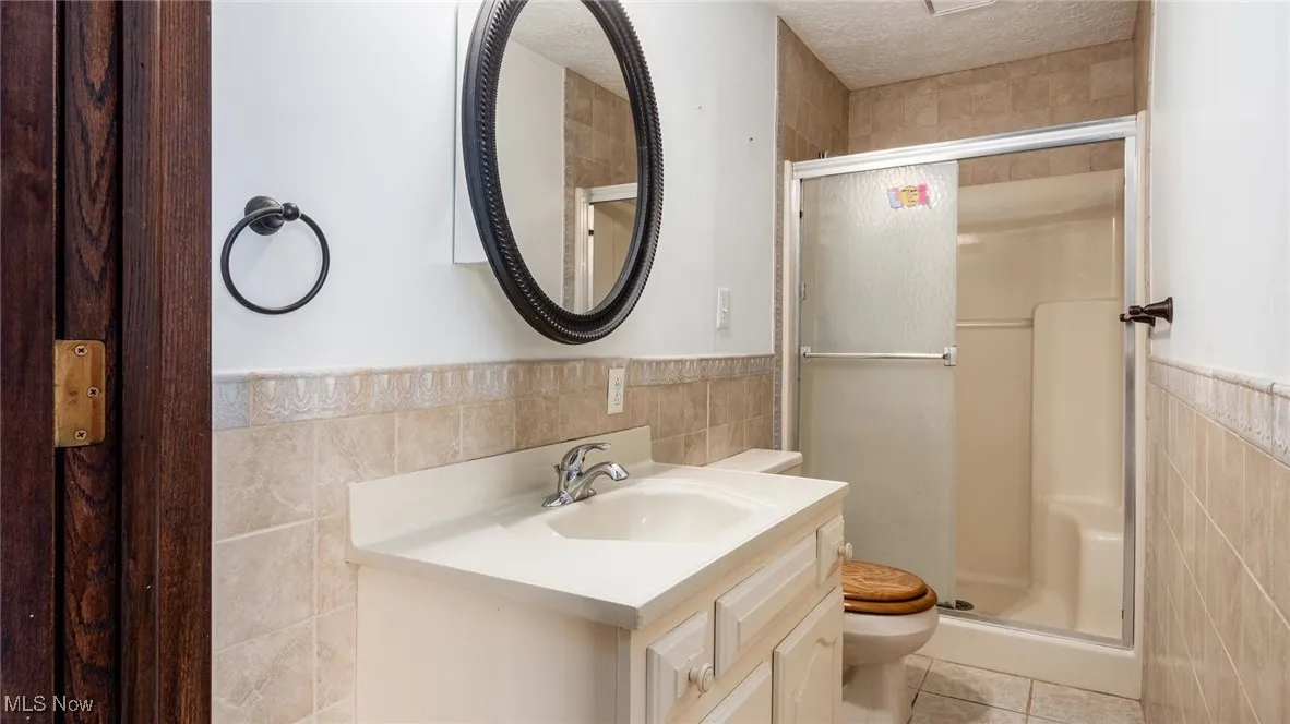 Bathroom featuring toilet, tile walls, a textured ceiling, vanity, and tile patterned flooring