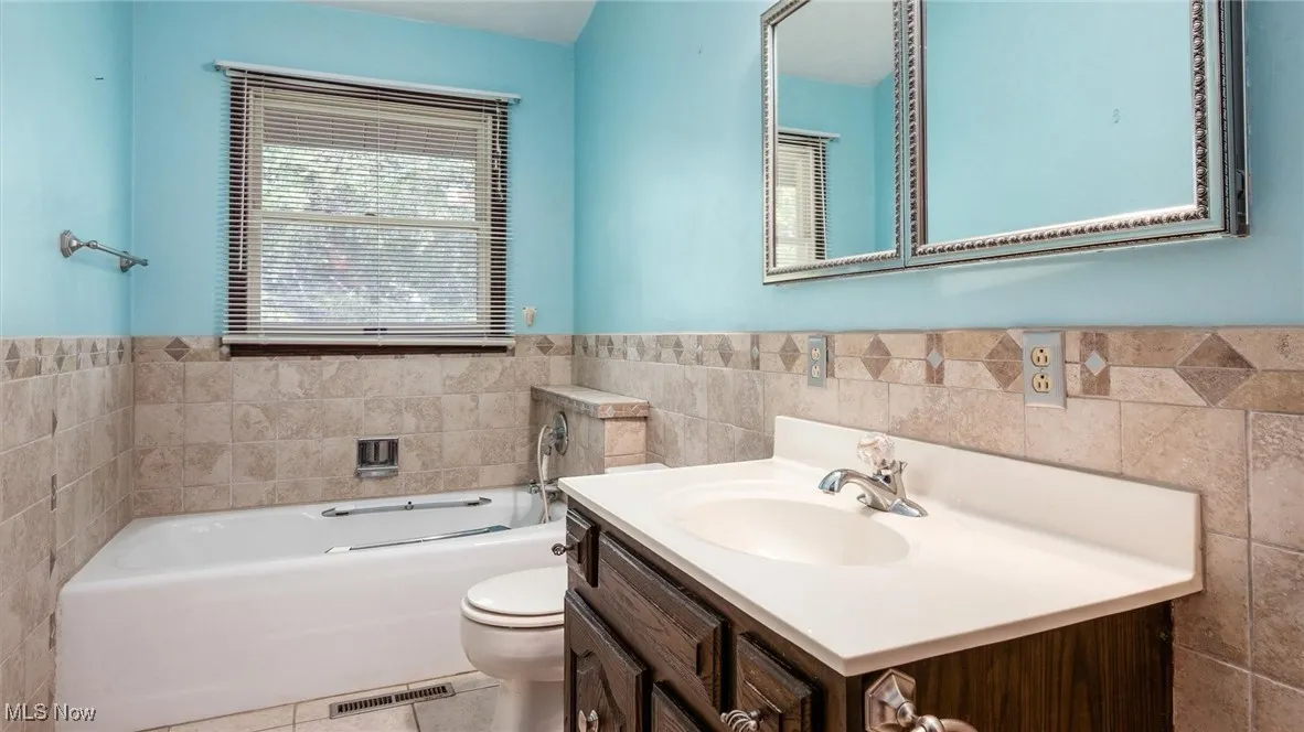 Bathroom featuring vanity, tile walls, a tub, and toilet