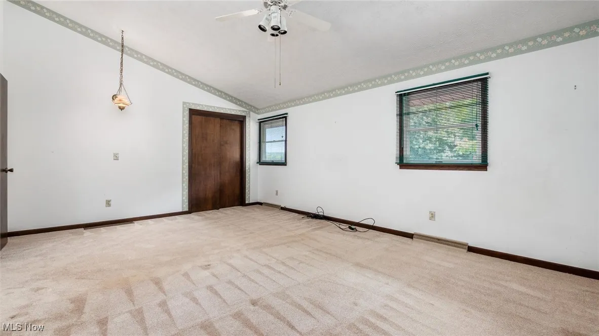 Carpeted empty room with lofted ceiling and ceiling fan