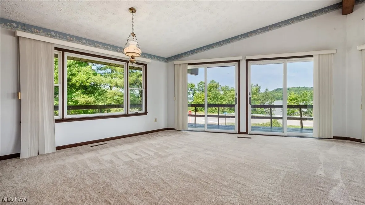 Empty room with a textured ceiling, vaulted ceiling, a healthy amount of sunlight, and carpet flooring