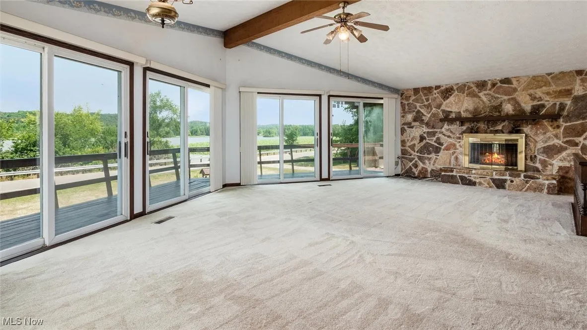 Unfurnished living room featuring ceiling fan, a fireplace, carpet floors, and vaulted ceiling with beams