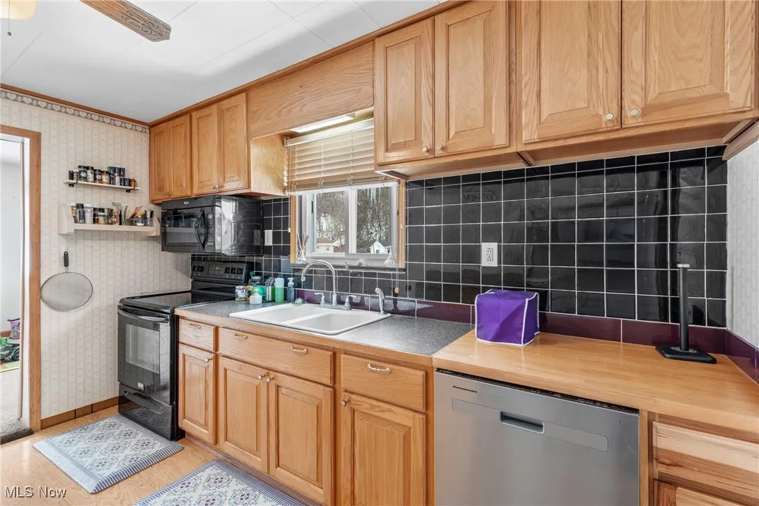Kitchen with sink, black appliances, light hardwood / wood-style flooring, ceiling fan, and backsplash