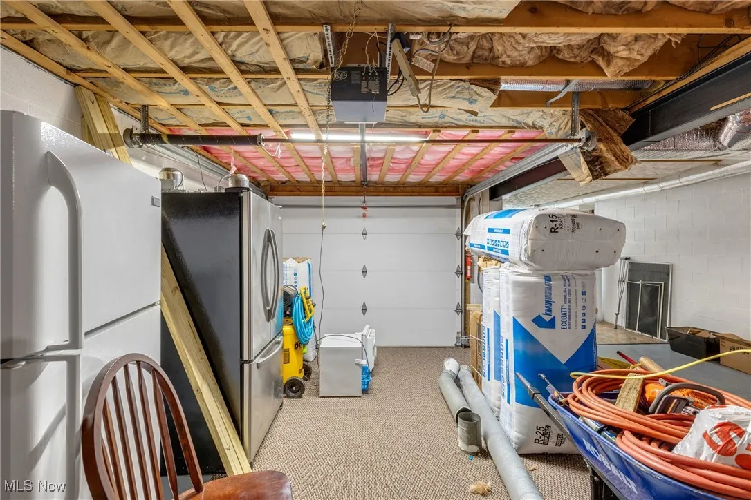 Garage with a garage door opener, stainless steel fridge, and white fridge
