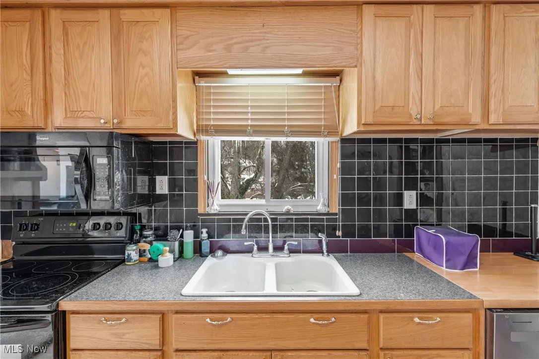Kitchen featuring sink, backsplash, and black appliances