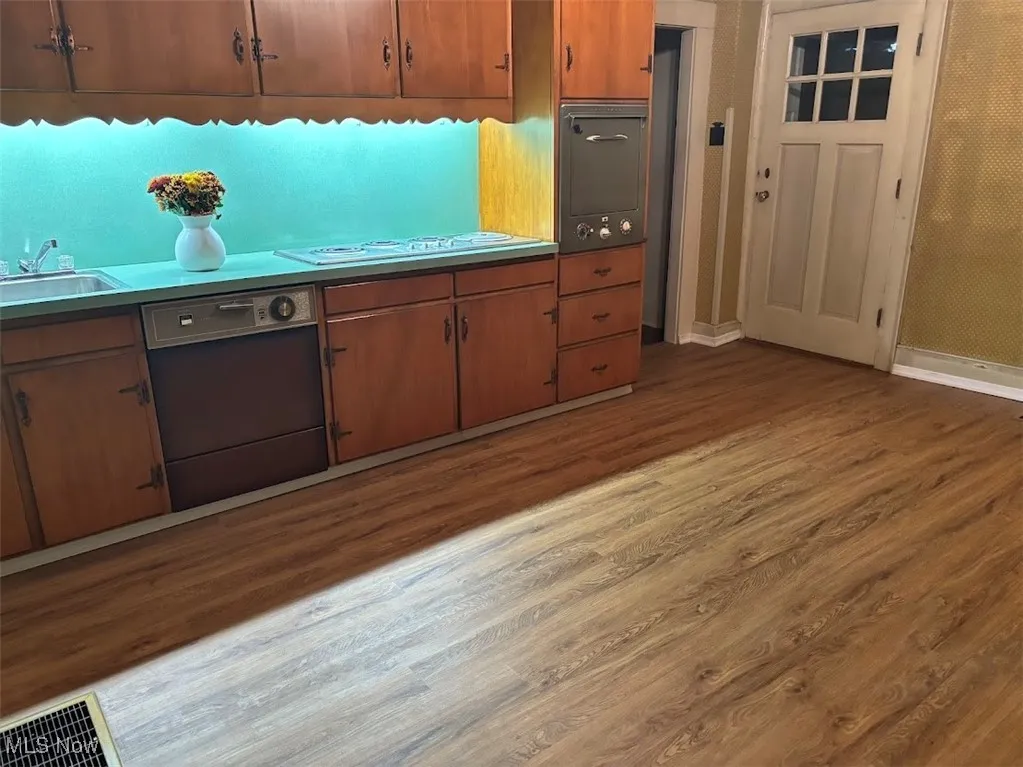 Kitchen with stovetop, dishwasher, hardwood / wood-style flooring, and sink