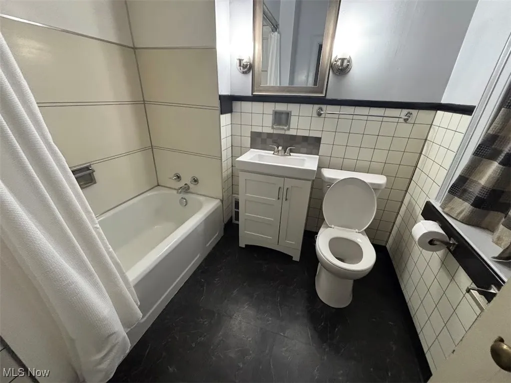 Full bathroom featuring shower / bath combination with curtain, vanity, toilet, and tile walls