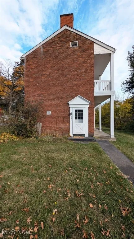 View of side of home featuring a yard and a balcony
