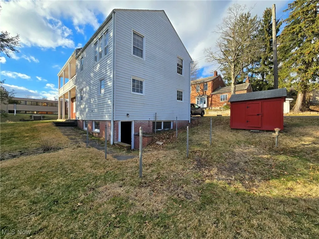 Back of property with a balcony, a storage unit, and a lawn