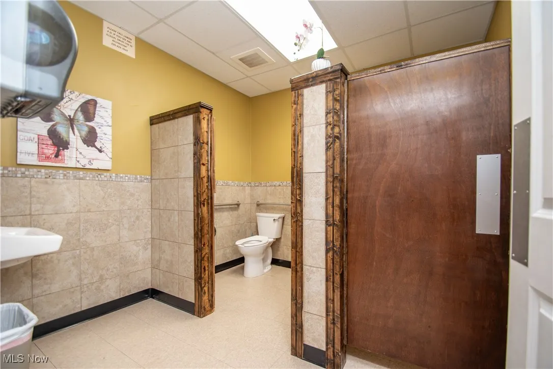 Bathroom featuring toilet, tile walls, and a drop ceiling