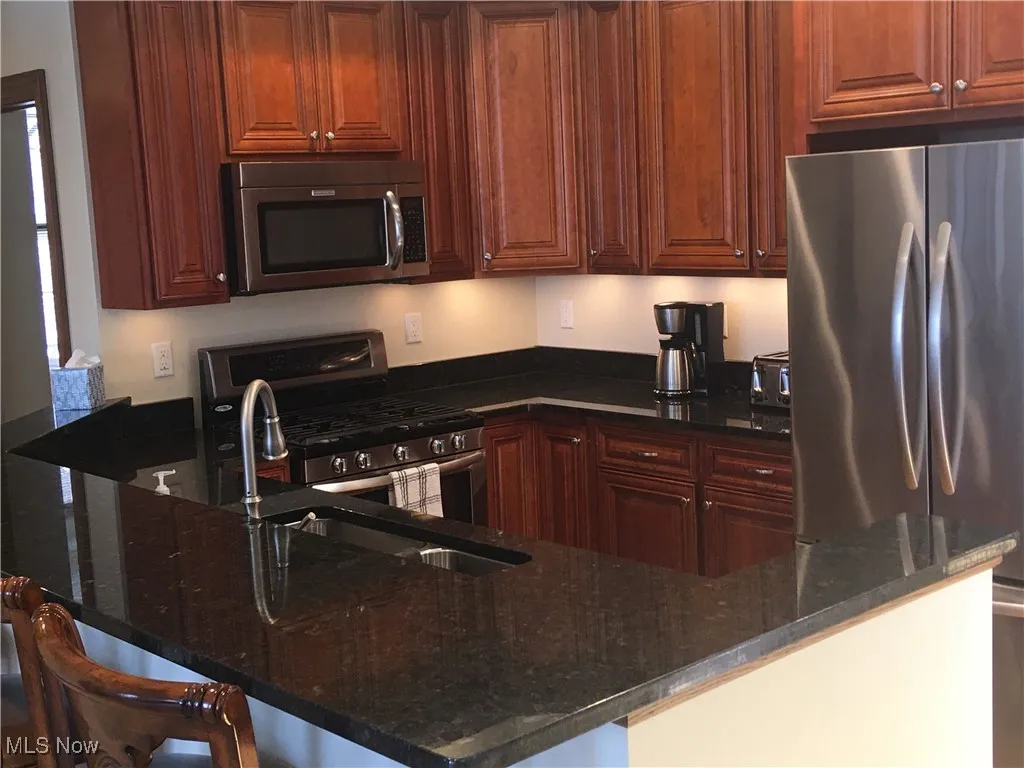 Kitchen with appliances with stainless steel finishes, sink, dark stone countertops, a breakfast bar area, and kitchen peninsula
