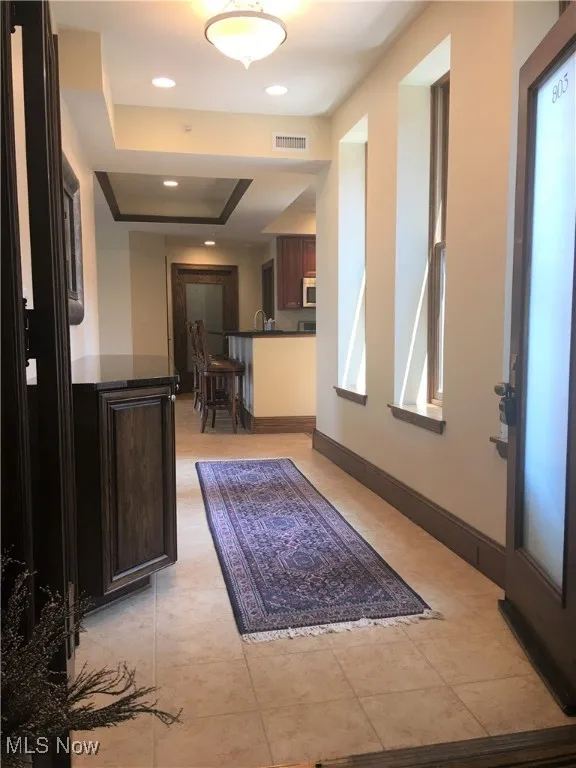 Corridor with light tile patterned flooring, a tray ceiling, and sink