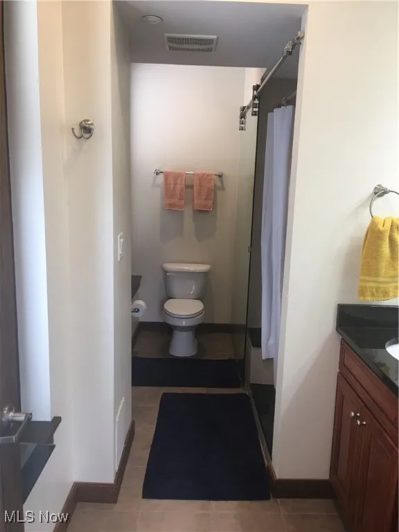 Bathroom featuring a shower with curtain, vanity, tile patterned floors, and toilet