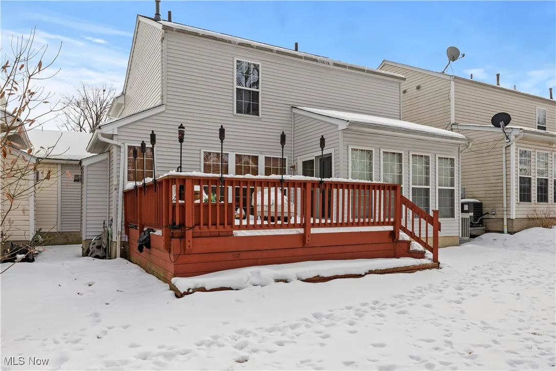 Snow covered back of property with a wooden deck and central AC unit
