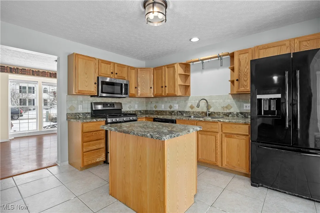 Kitchen with sink, dark stone counters, a center island, light tile patterned floors, and black appliances