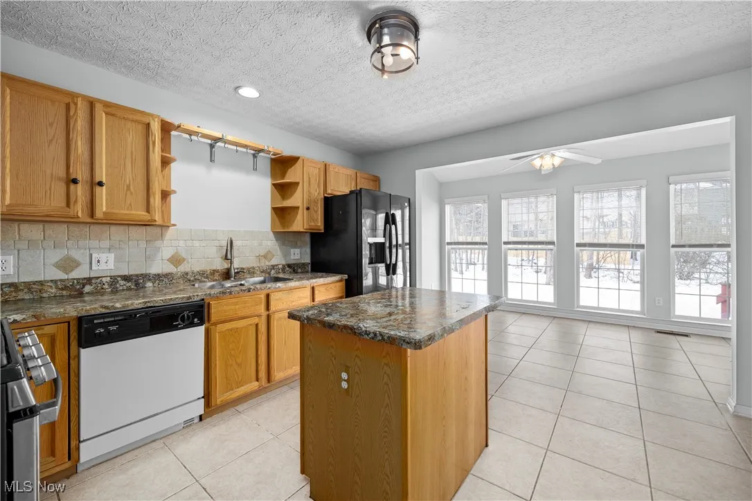 Kitchen featuring black fridge with ice dispenser, sink, tasteful backsplash, a center island, and dishwasher