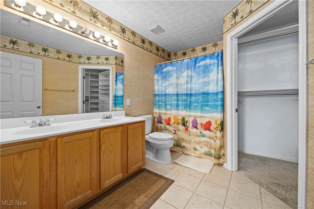 Bathroom with tile patterned floors, vanity, toilet, and a textured ceiling