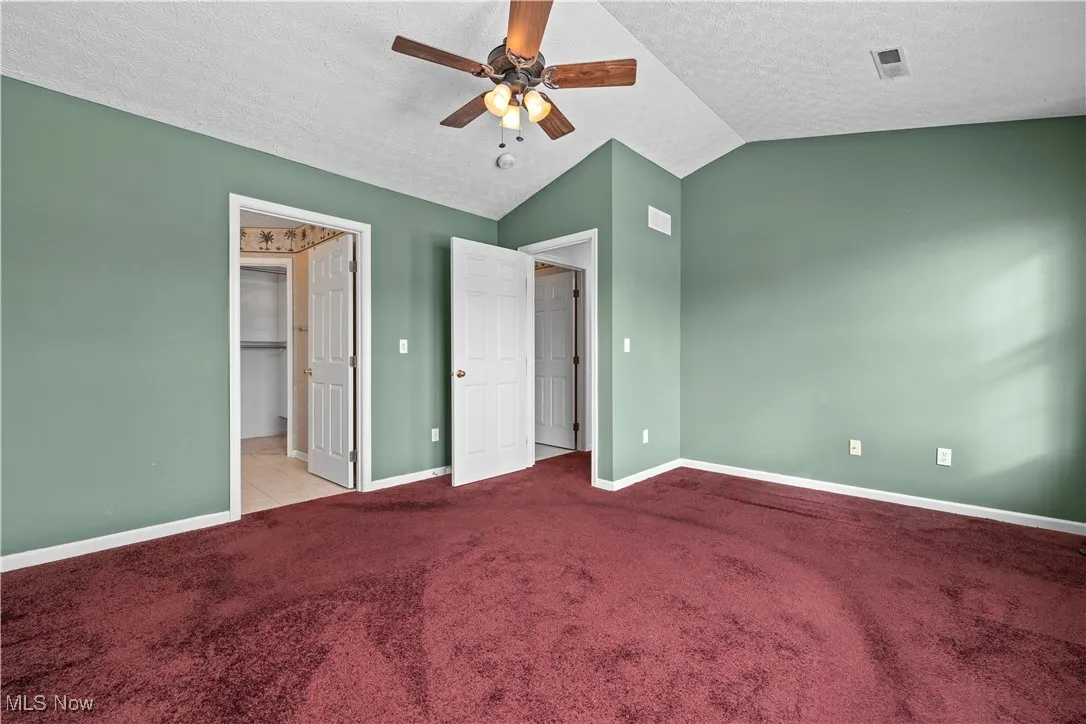 Unfurnished bedroom with lofted ceiling, ceiling fan, light colored carpet, and a textured ceiling