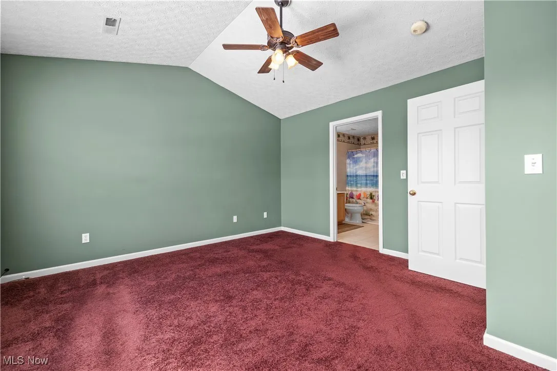 Carpeted empty room with lofted ceiling, a textured ceiling, and ceiling fan