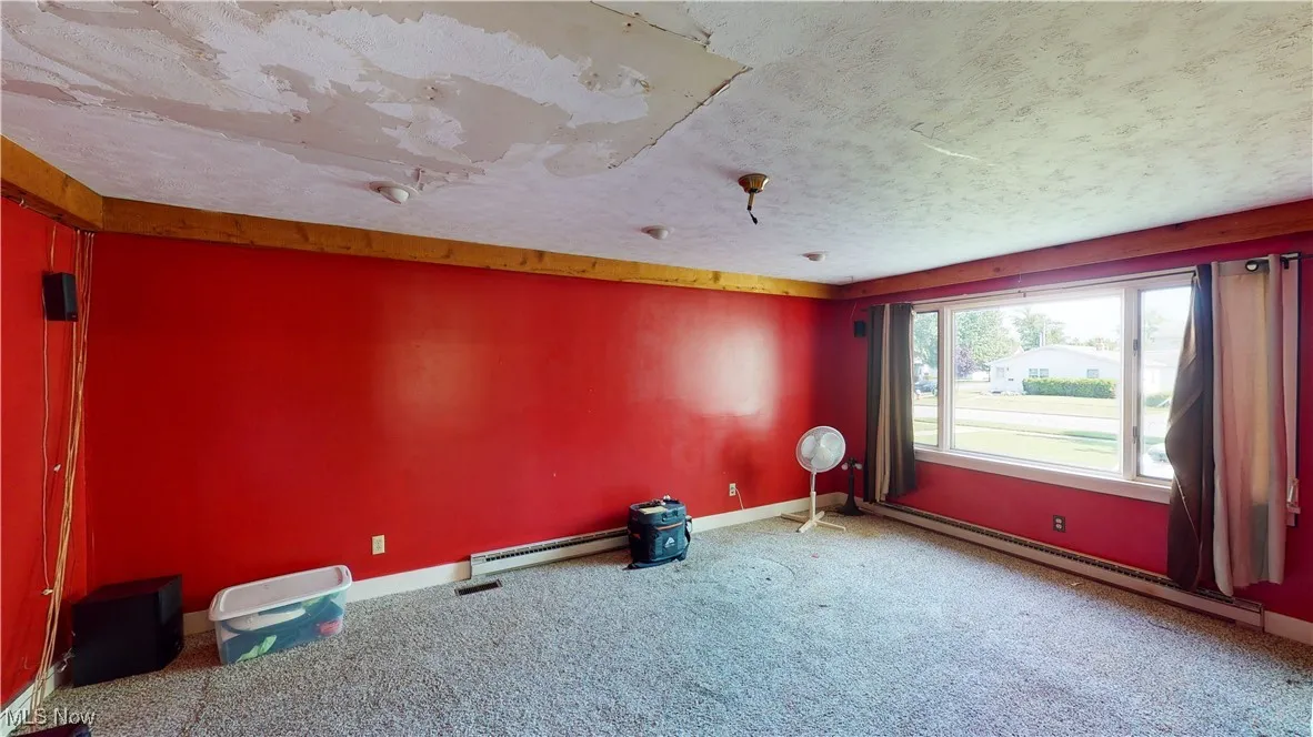 Carpeted empty room featuring a textured ceiling and a baseboard heating unit