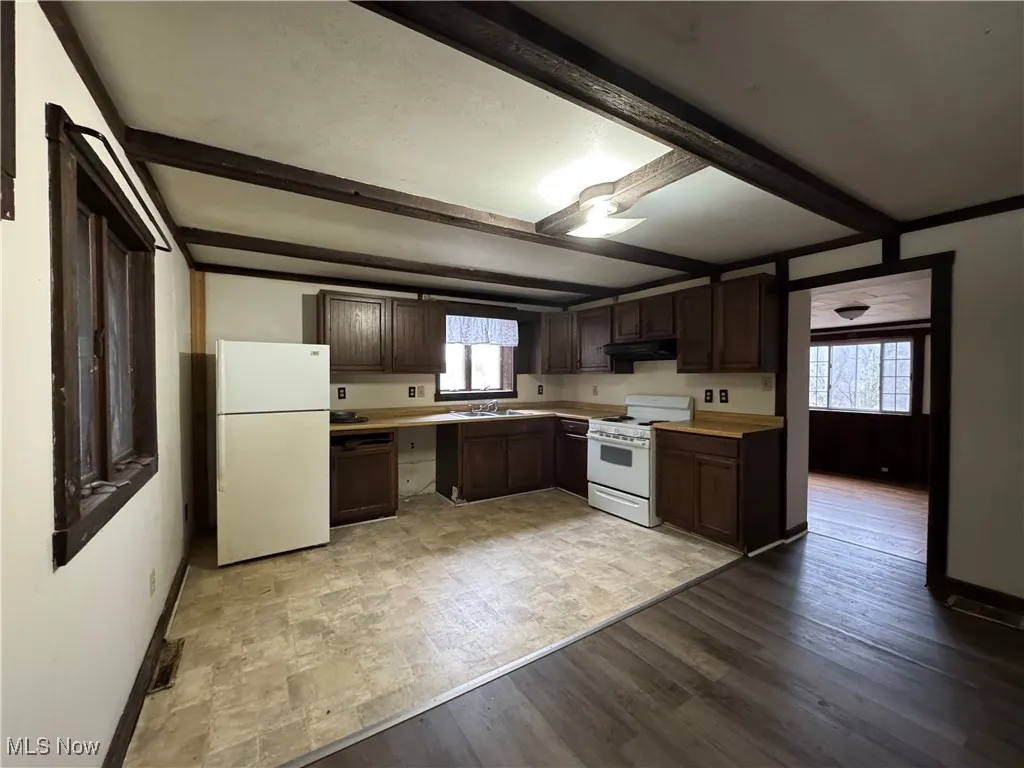 Kitchen with beamed ceiling, white appliances, dark brown cabinets, and light hardwood / wood-style flooring