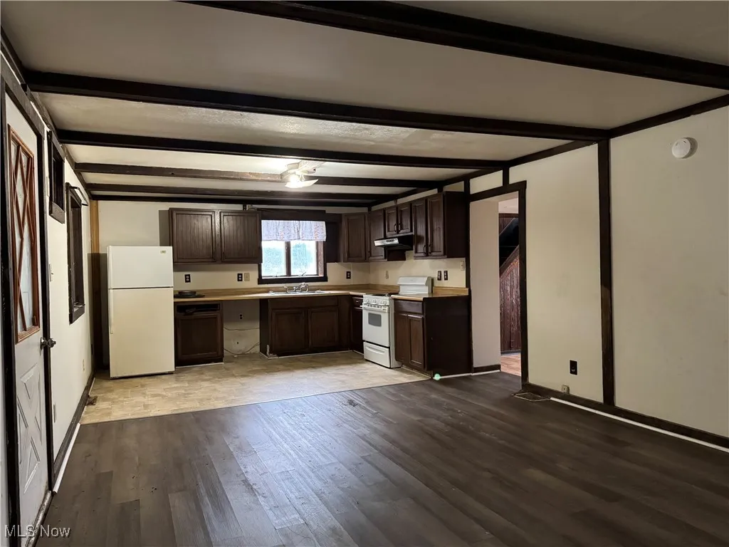 Kitchen featuring light wood-type flooring, sink, white appliances, dark brown cabinets, and beam ceiling
