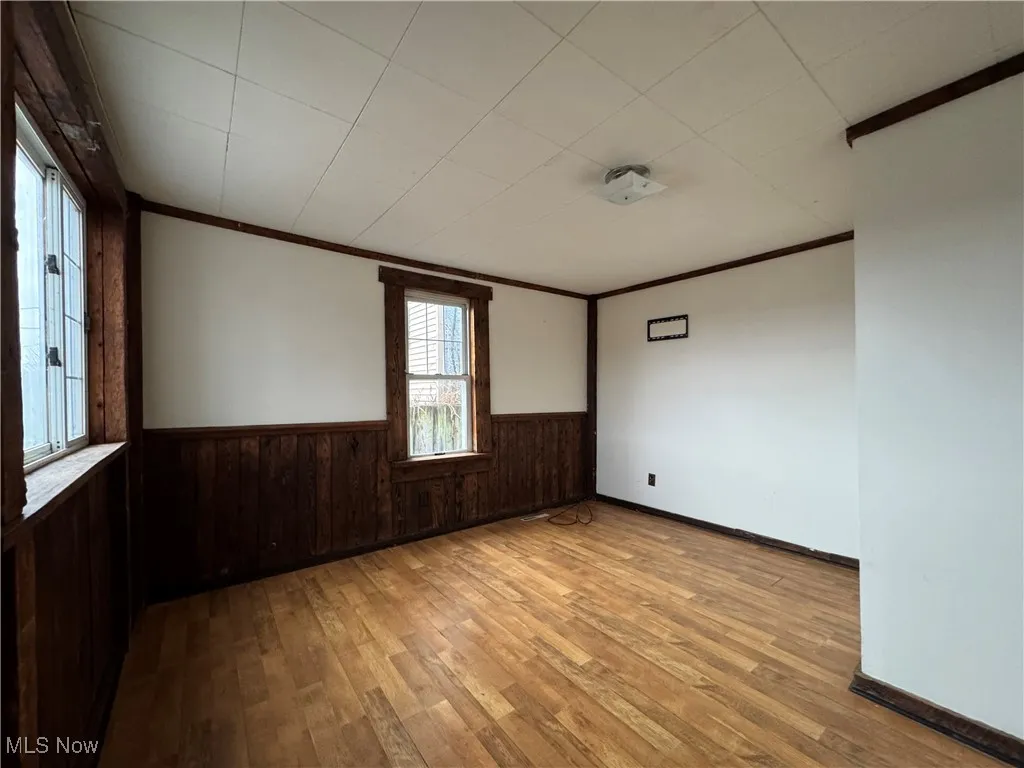 Unfurnished room with ornamental molding, light hardwood / wood-style flooring, and wood walls