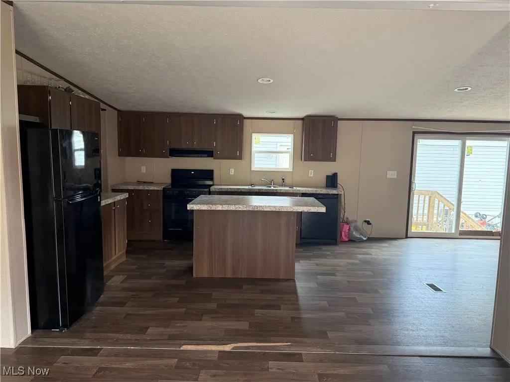Kitchen featuring black appliances, under cabinet range hood, light countertops, a kitchen island, and dark wood-type flooring