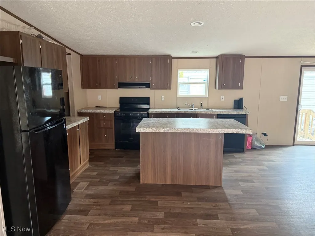 Kitchen featuring black appliances, ventilation hood, dark wood-style flooring, light countertops, and a textured ceiling