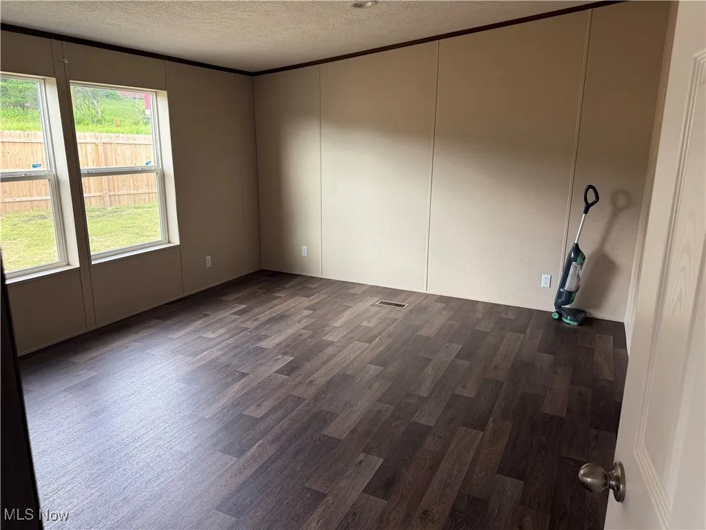 Spare room featuring a textured ceiling, dark wood-style flooring, and a decorative wall