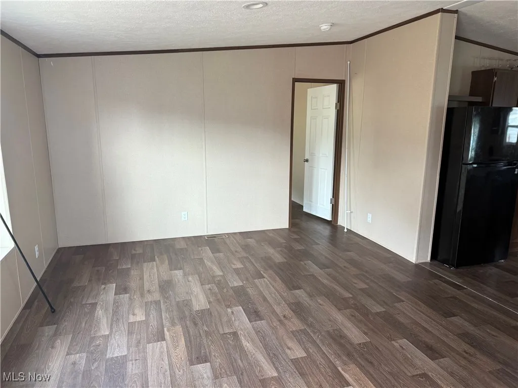Empty room with ornamental molding, dark wood-type flooring, a textured ceiling, a decorative wall, and a smoke detector