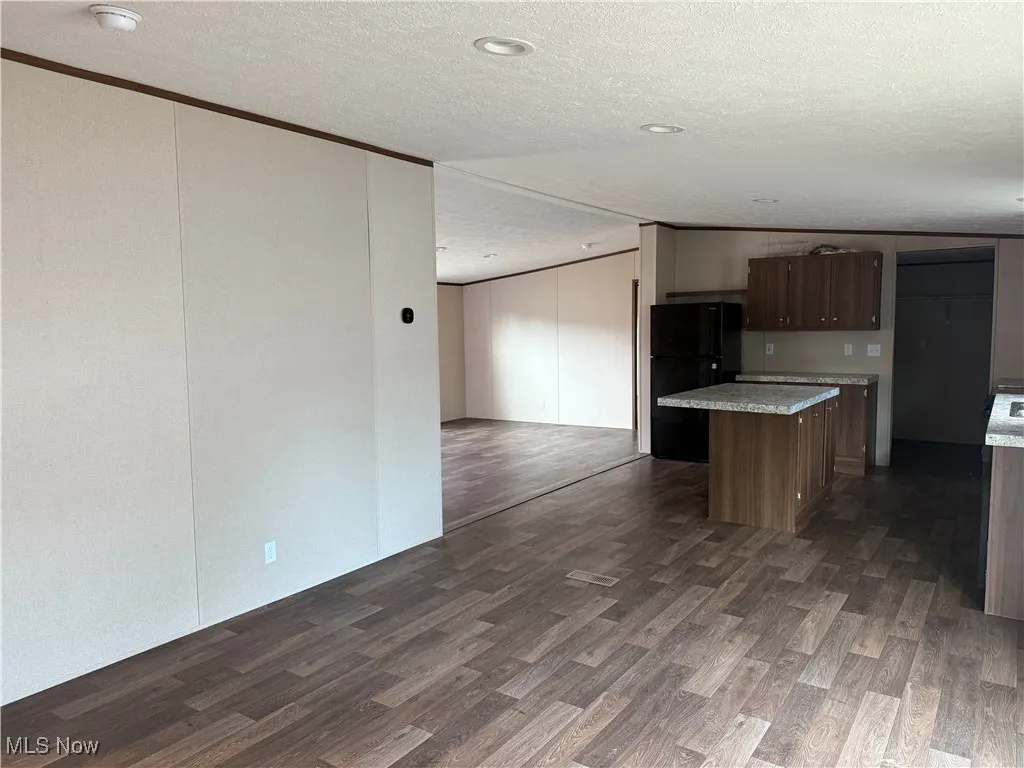 Kitchen with freestanding refrigerator, a center island, dark wood finished floors, a textured ceiling, and crown molding