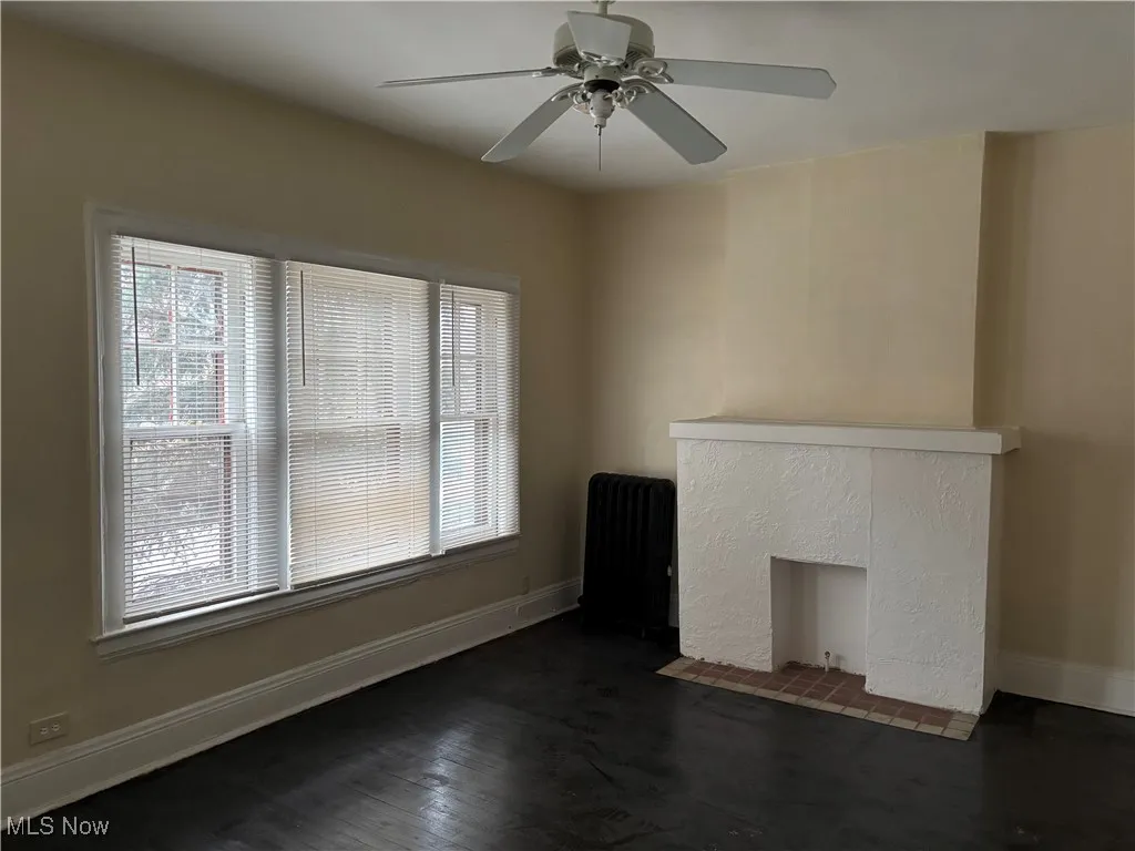 Unfurnished living room with a tiled fireplace, plenty of natural light, radiator, and dark hardwood / wood-style floors