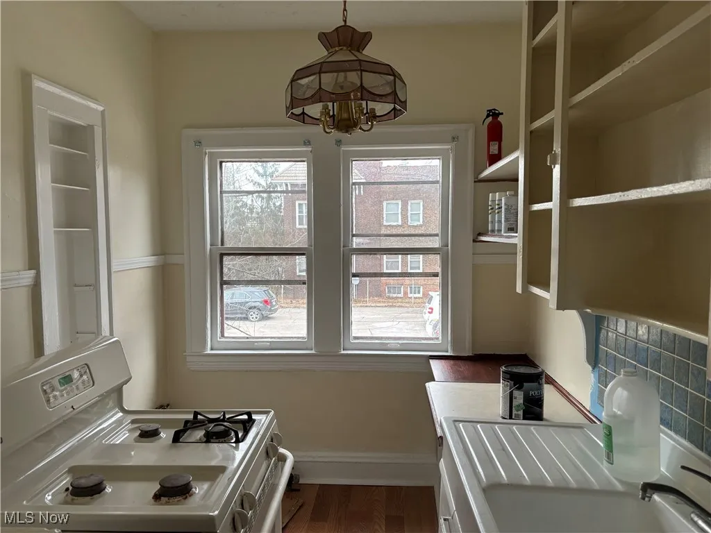 Kitchen featuring sink, white gas range oven, decorative backsplash, dark hardwood / wood-style flooring, and decorative light fixtures