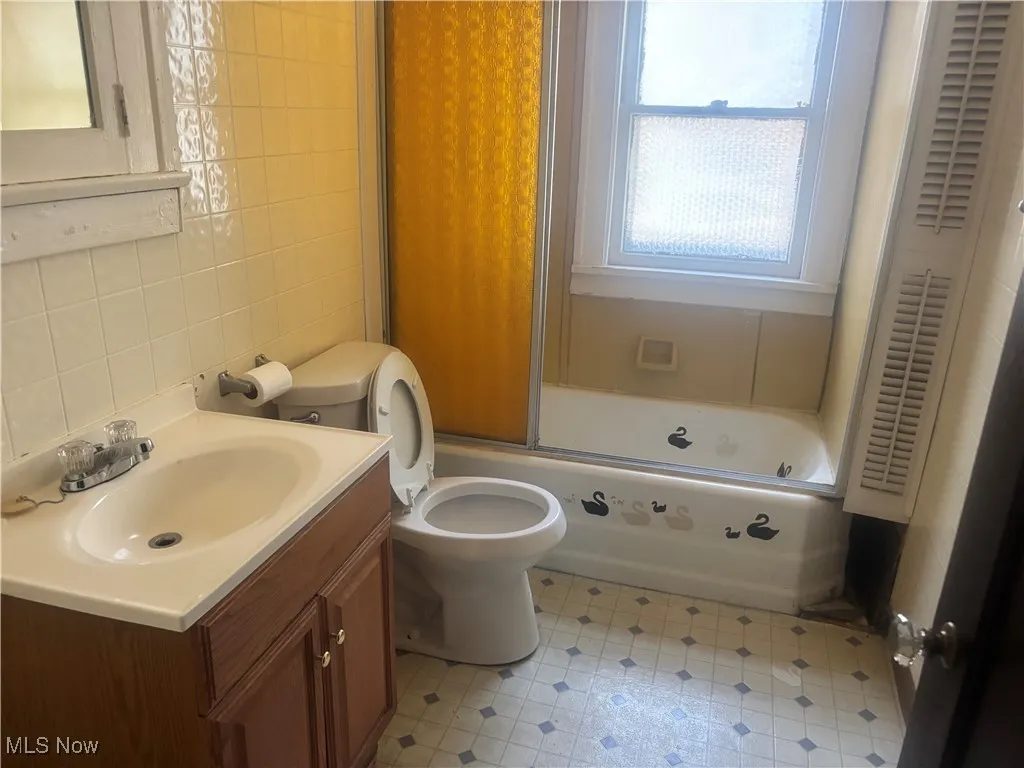 Full bath with decorative backsplash, tile walls, vanity, toilet, and enclosed tub / shower combo