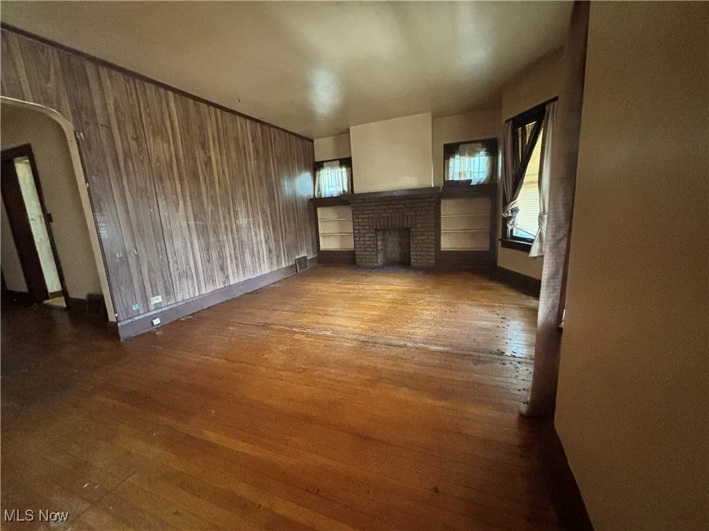 Unfurnished living room with a fireplace, arched walkways, visible vents, and hardwood / wood-style floors