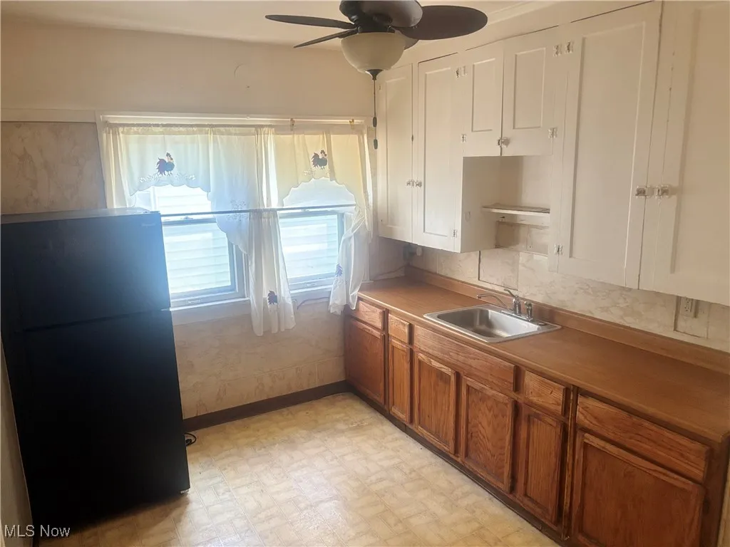 Kitchen with brown cabinetry, freestanding refrigerator, light floors, ceiling fan, and a sink