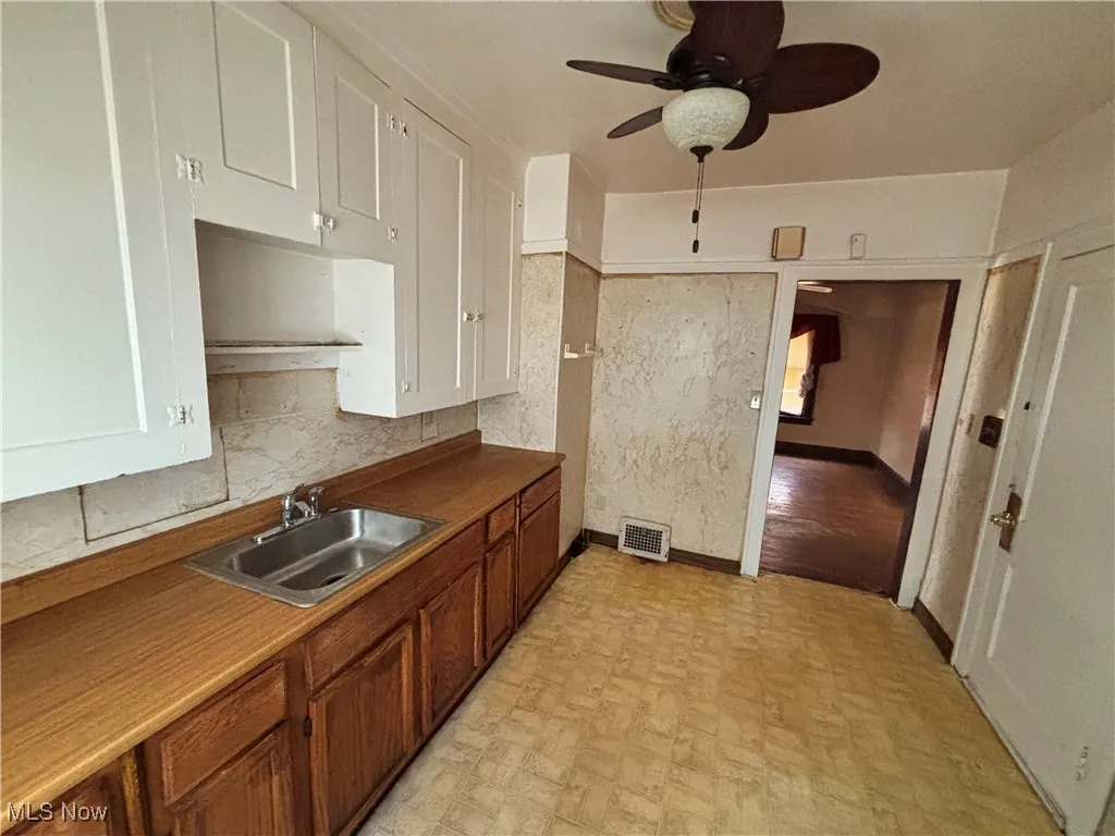 Kitchen featuring visible vents, a ceiling fan, brown cabinetry, baseboards, and a sink