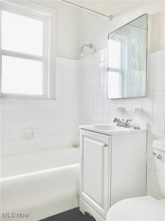 Full bathroom featuring vanity, tiled shower / bath, toilet, and tile walls