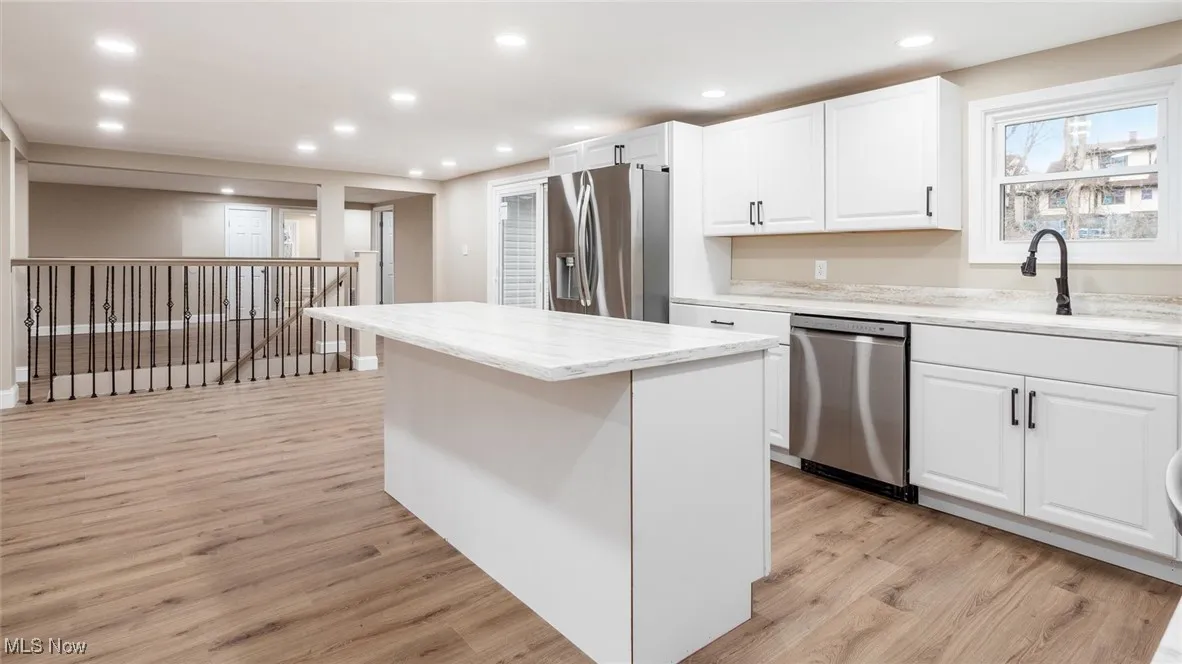 Kitchen with white cabinetry, light stone counters, a center island, stainless steel appliances, and light hardwood / wood-style floors