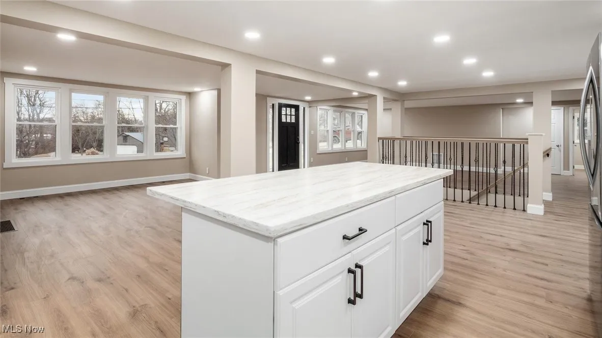 Kitchen with white cabinetry, a kitchen island, light wood-type flooring, and light stone counters