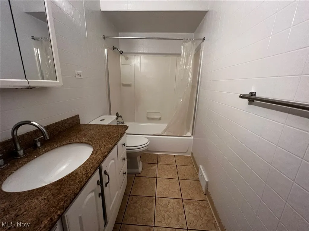 Full bathroom featuring shower / tub combo with curtain, tile patterned floors, toilet, tile walls, and vanity