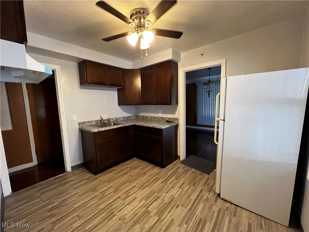 Kitchen with sink, ceiling fan, dark brown cabinets, white refrigerator, and light stone counters