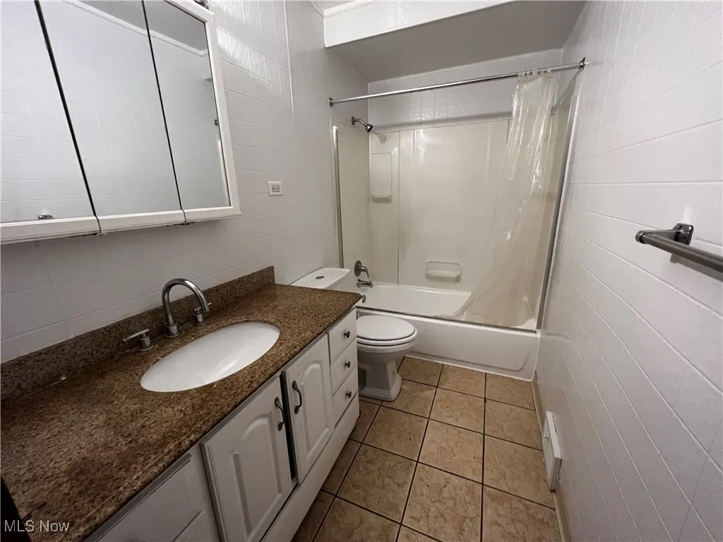 Full bathroom featuring tile walls, vanity, toilet, shower / bathtub combination with curtain, and tile patterned floors
