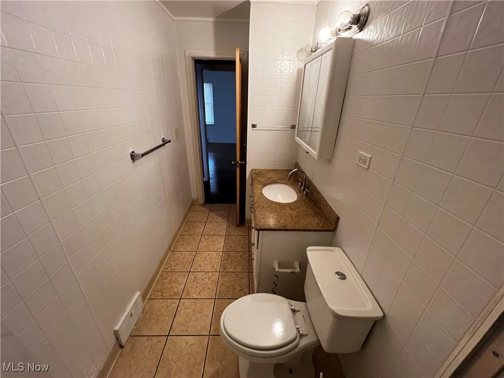 Bathroom featuring tile patterned flooring, vanity, tile walls, and toilet