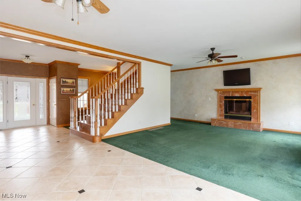 Unfurnished living room featuring ceiling fan, a high end fireplace, ornamental molding, and carpet floors