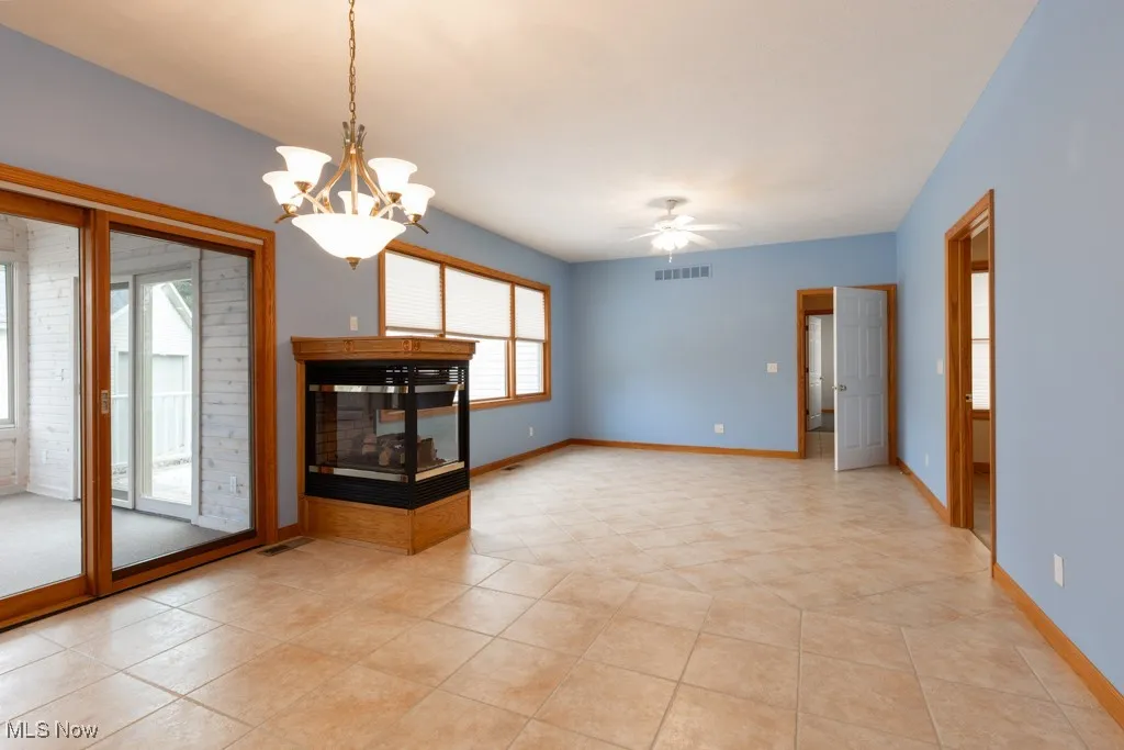 Unfurnished living room featuring a multi sided fireplace, ceiling fan with notable chandelier, and light tile patterned floors