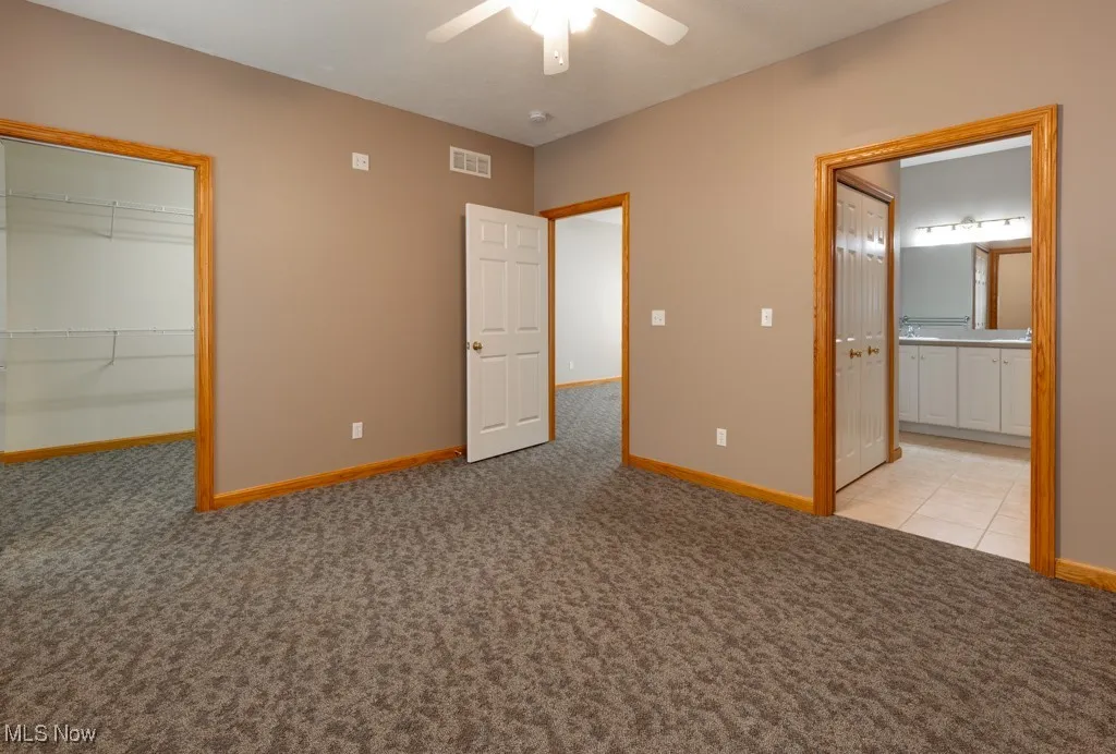 Unfurnished bedroom with ensuite bath, a spacious closet, light colored carpet, a closet, and ceiling fan