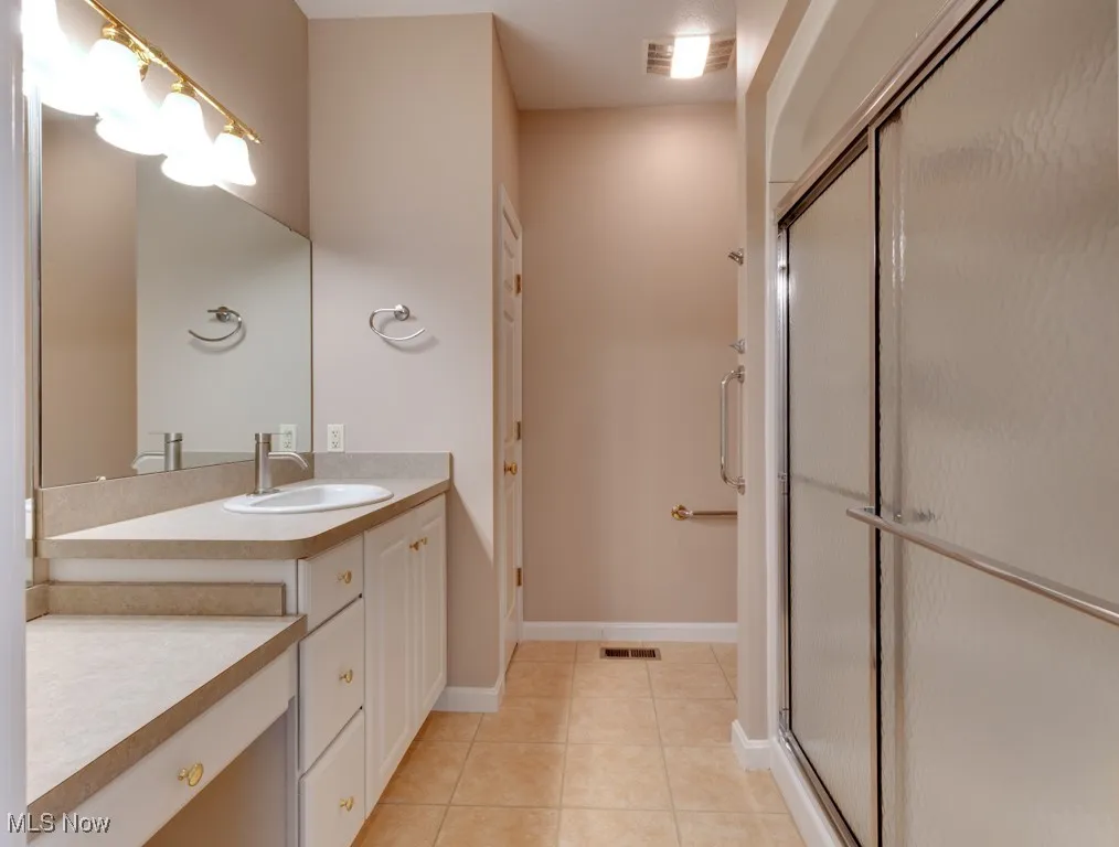 Bathroom with tile patterned floors, a shower with door, and vanity