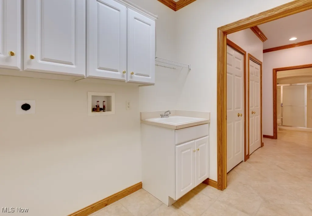 Clothes washing area featuring sink, crown molding, electric dryer hookup, hookup for a washing machine, and cabinets